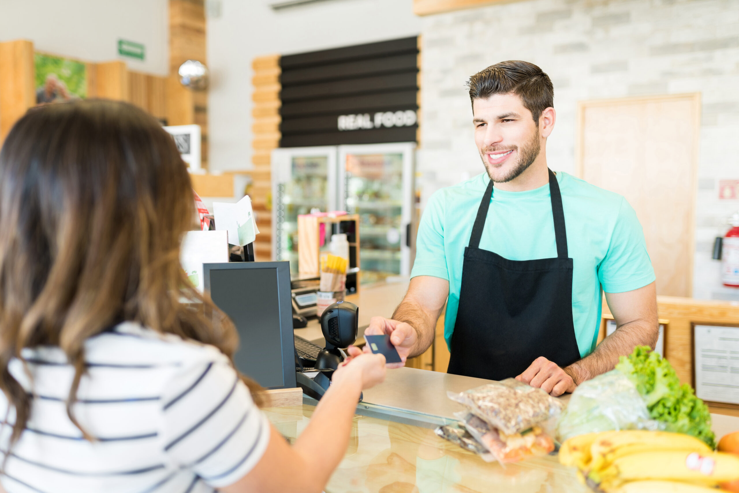 smiling male cashier receiving payment through credit card supermarket scaled